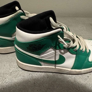 Nike Air Jordans i grönt och vitt - Snygga Nike Air Jordans i en fräsch grön och vit färgkombination. Skorna har klassisk snörning och en hög siluett som ger ett sportigt utseende. Perfekta för dig som vill ha en stilren och ikonisk sneaker.