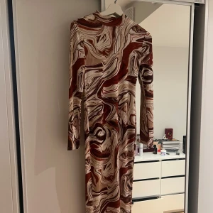 Mönstrad långärmad klänning - Säljer en cool långärmad klänning med ett abstrakt mönster i brunt, beige och vitt. Klänningen har en tight passform och är perfekt för att sticka ut. Den är gjord i ett mjukt och stretchigt material som formar sig efter kroppen.