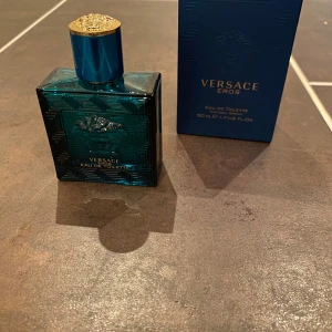 Versace Eros Eau de Toilette 50 ml - Säljer en flaska Versace Eros Eau de Toilette, 50 ml. Flaskan är i en djupblå färg med ett elegant mönster och Versaces ikoniska Medusa-logga. Den har en gyllene kork som ger en lyxig känsla. Perfekt för den som vill ha en doft med karaktär och stil.