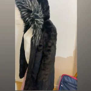 Svart pälsjacka med huva - Säljer en svart pälsjacka med fluffig huva. Jackan har långa ärmar och är perfekt för kyliga dagar. Den är stilren och mysig, med en lyxig känsla tack vare den mjuka pälsen.