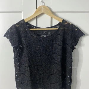 Svart spetsblus  - Snygg svart spetsblus från Camaïeu med korta ärmar. Perfekt för att ge en elegant touch till din outfit. Blusen har en rund halsringning och är tillverkad i ett vackert spetsmaterial. Jättefin och stilig!