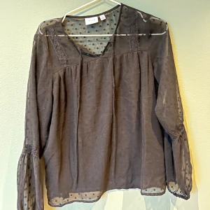 Svart blus från Vila - Snygg svart blus från Vila med prickigt mönster och v-ringad design. Blusen har långa ärmar och spetsdetaljer vid axlarna💕