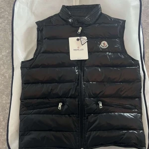 Svart dunväst  - Säljer en snygg svart dunväst med dragkedja och två fickor framtill. Västen har en quiltad design. Perfekt för kyligare dagar! Eller på sommarkvällar! Om ni undrar något bara hör av er!