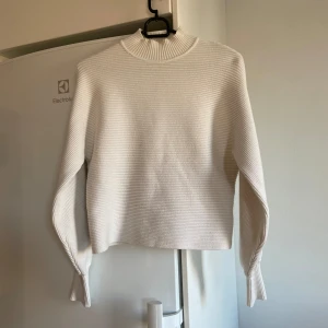 Vit ribbad tröja från Zara - Säljer en superfin vit ribbad tröja från Zara i storlek S. Den har en halvhög krage och långa ärmar med snygga detaljer längs sidorna. Perfekt för både höst och vinter, och den är i nyskick! Det är en liten fläck tror ja sista bilden (inget som syns)