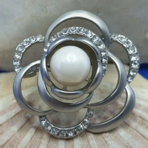 Brosch  - Kamelia blomma i silver kulör. - En brosch föreställande en Kamelia blomma, storlek ca 4.5x4.5cm.  Silverfärgad metall med vacker ytstruktur och genombruten yta med kristaller och en större pärla.  Grymt snygg brosch.