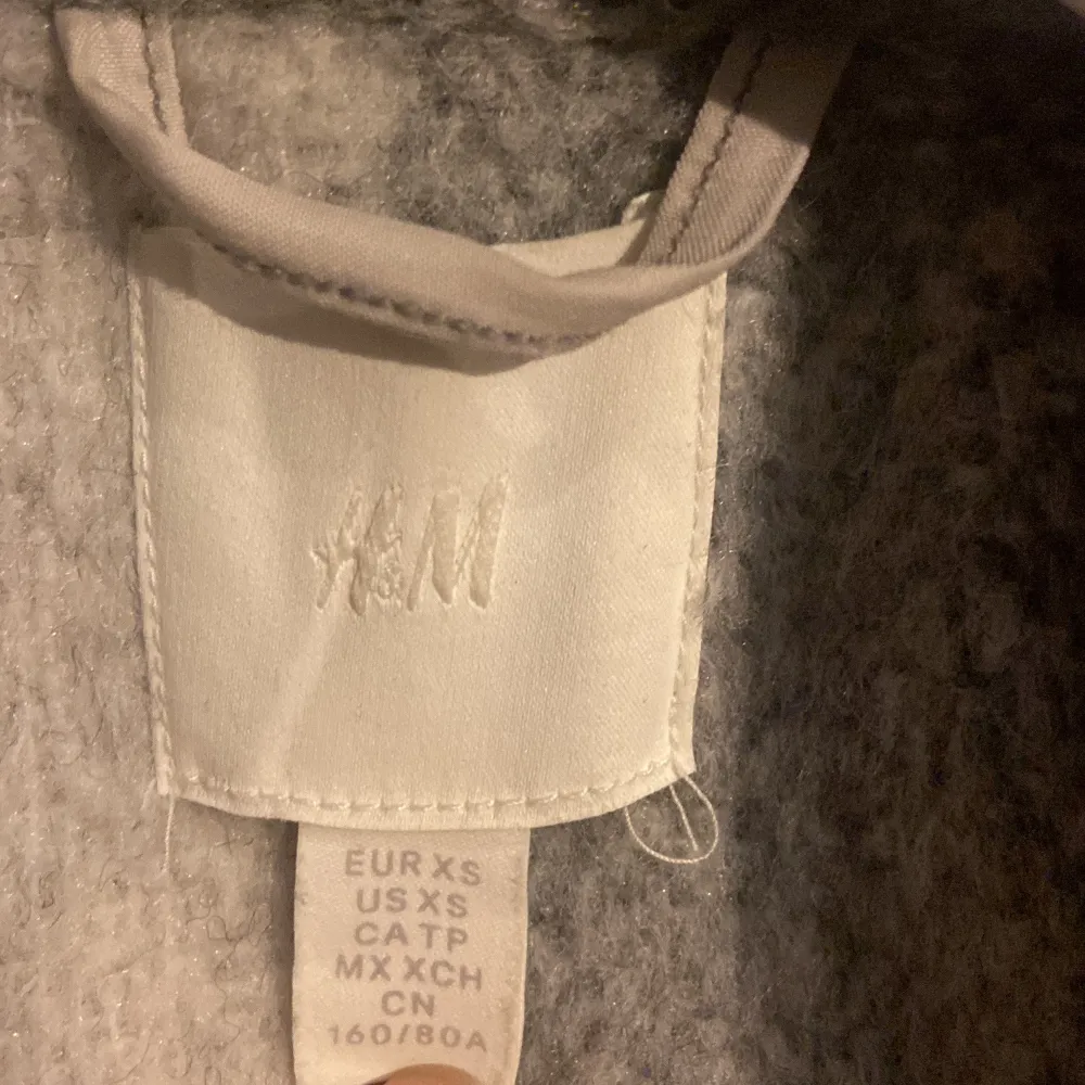 Säljer en superfin grå och vit rutig kappa från H&M. Den är i storlek XS och har en klassisk stil med långa ärmar och knappar framtill. Perfekt för höst och vinter när du vill hålla dig varm och snygg. Kappan är i bra skick och redo för nya äventyr!. Takit.