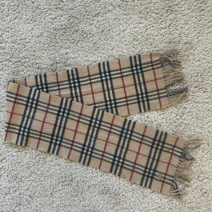Burberry Halsduk - En riktigt skön och snygg burberry halsduk som är i bra skick men den har ett litet hål som man ser på andra bilden. Halsduken är äkta 
