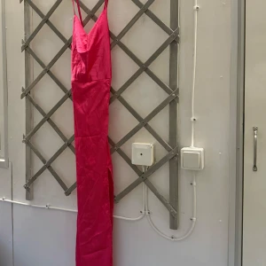Klänning shein - En vacker klänning i en härlig rosa färg. Den har en djup urringning framtill och en öppen rygg med snörning. Klänningen är figursydd och har en slits i sidan. Den är aldrig använd och är från Shein!