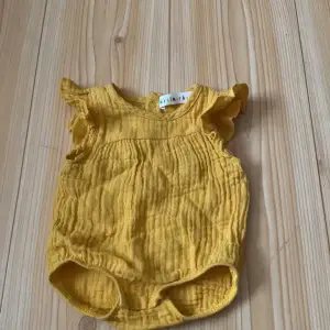 Säljer en supergullig gul babybody från Minimarket i storlek 44. Den är gjord av mjukt och bekvämt material, perfekt för de minsta. Bodyn har söta volangdetaljer vid ärmarna och praktiska tryckknappar i grenen för enkel på- och avklädning. Perfekt för sommarens varma dagar! 🌞