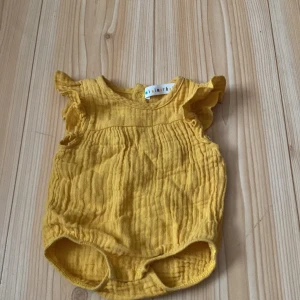 Gul babybody från Minimarket - Säljer en supergullig gul babybody från Minimarket i storlek 44. Den är gjord av mjukt och bekvämt material, perfekt för de minsta. Bodyn har söta volangdetaljer vid ärmarna och praktiska tryckknappar i grenen för enkel på- och avklädning. Perfekt för sommarens varma dagar! 🌞