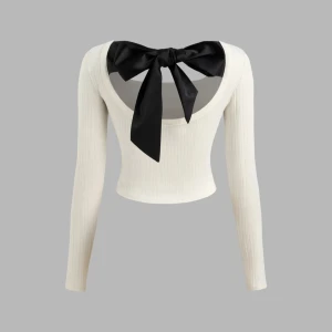 Vit ribbad topp med svart rosett - Säljer en superfin vit ribbad topp med långärmade ärmar. Toppen har en öppen rygg med en stor svart rosett som detalj. Perfekt för både vardag och fest!