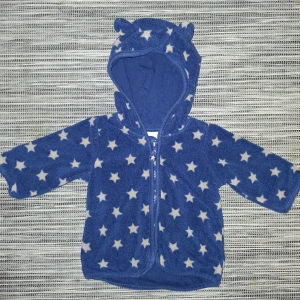Blå fleecejacka med stjärnor från H&M - Söt blå fleecejacka från H&M med vita stjärnor och huva med små öron. Perfekt för att hålla de små varma och mysiga. Jackan har en dragkedja framtill för enkel på- och avtagning. Storlek 62 i nästintill nyskick!