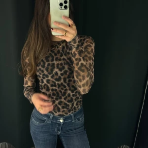 Leopardmönstrad långärmad body - Snygg leopardmönstrad body med långa ärmar. Perfekt för att ge din outfit en trendig touch. Passar bra till jeans eller kjol för en cool look.