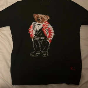 Svart tröja med nallemotiv från Ralph Lauren - Säljer en svart stickad polo Björn tröja. Den är storlek S skulle passa på någon som är runt 170. Är i skick 8/10. Priset är inte fast kan betalas mindre vid snabb affär.