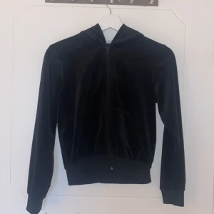 Svart ziptröja från Kappahl - Säljer en svart mjuk zip-tröja från Kappahl med dragkedja och huva. Jackan har långa ärmar och en mjuk känsla, perfekt för en avslappnad stil. Passar bra för både höst och vår.