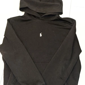 Svart hoodie från Polo Ralph Lauren - Säljer en stilren svart hoodie från Polo Ralph Lauren med det klassiska logotypbroderiet på bröstet. Perfekt för en avslappnad look. Hoodien har en bekväm passform och är tillverkad i mjukt material.