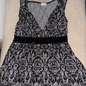 Svart och vit klänning från Limited Edition Kappahl - Elegant svart och vit klänning med ett intrikat mönster och en v-ringad design. Klänningen har en dekorativ paljettbård i midjan som ger en extra touch av glamour. Perfekt för speciella tillfällen.