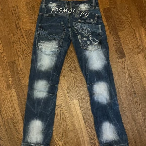 Kosmolupo jeans - Snygga blå jeans från K&M Jeans med unika broderade detaljer och slitna effekter. Byxorna har flera fickor och en cool design med texten 'Kosmo lupo. Skriv för fler frågor eller bilder🎀🩷