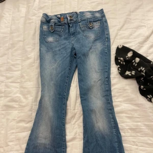 Blå bootcut jeans från Pulz Jeans - Snygga blå bootcut jeans från Pulz Jeans med en klassisk femficksdesign. Jeansen har en lätt slitning för en trendig look och är perfekta för en vardags outfit. De har en knapp- och dragkedjestängning framtill.