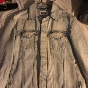 Ljusblå jeansjacka från Weekday - Snygg ljusblå jeansjacka från Weekday med klassisk design. Jackan har knappar framtill och två bröstfickor med lock. Perfekt för en avslappnad stil.