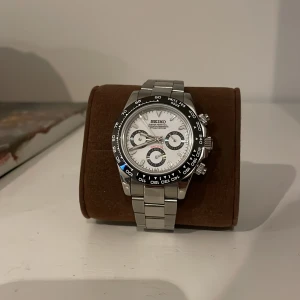 Silverfärgad klocka från Seiko daytona. - Snygg silverfärgad klocka från Seiko med vit urtavla och tre sub-dials. Klockan har en robust metallarmband och en svart bezel med vita markeringar. Perfekt för den som gillar en klassisk och stilren design med hög kvalitet till fint pris:). Inga anmärkningsbara repor eller annat, som ny. Köpt här på plick för 4000kr.