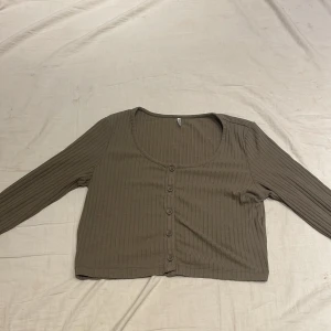 Grön ribbad kofta - Säljer en stilren grön ribbad kofta med knappar framtill. Koftan har en rund halsringning och långa ärmar, perfekt för lager på lager-stil. Passar bra till både jeans och kjol. Perfekt för höst och vår!