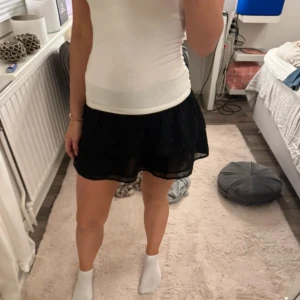 Svart kortkjol - Snygg svart kortkjol med volangdetaljer från Gina tricot. Perfekt för att ge en stilfull touch till din outfit. Kjolen är i storlek xs men passar även xxs. 