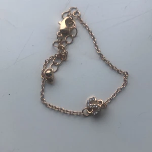 Guldarmband med gnistrande detalj - Elegant guldarmband med en gnistrande detalj i form av en bokstav. Armbandet har en fin kedja och justerbar längd med en säker låsning. Perfekt för att ge en personlig touch till din stil.