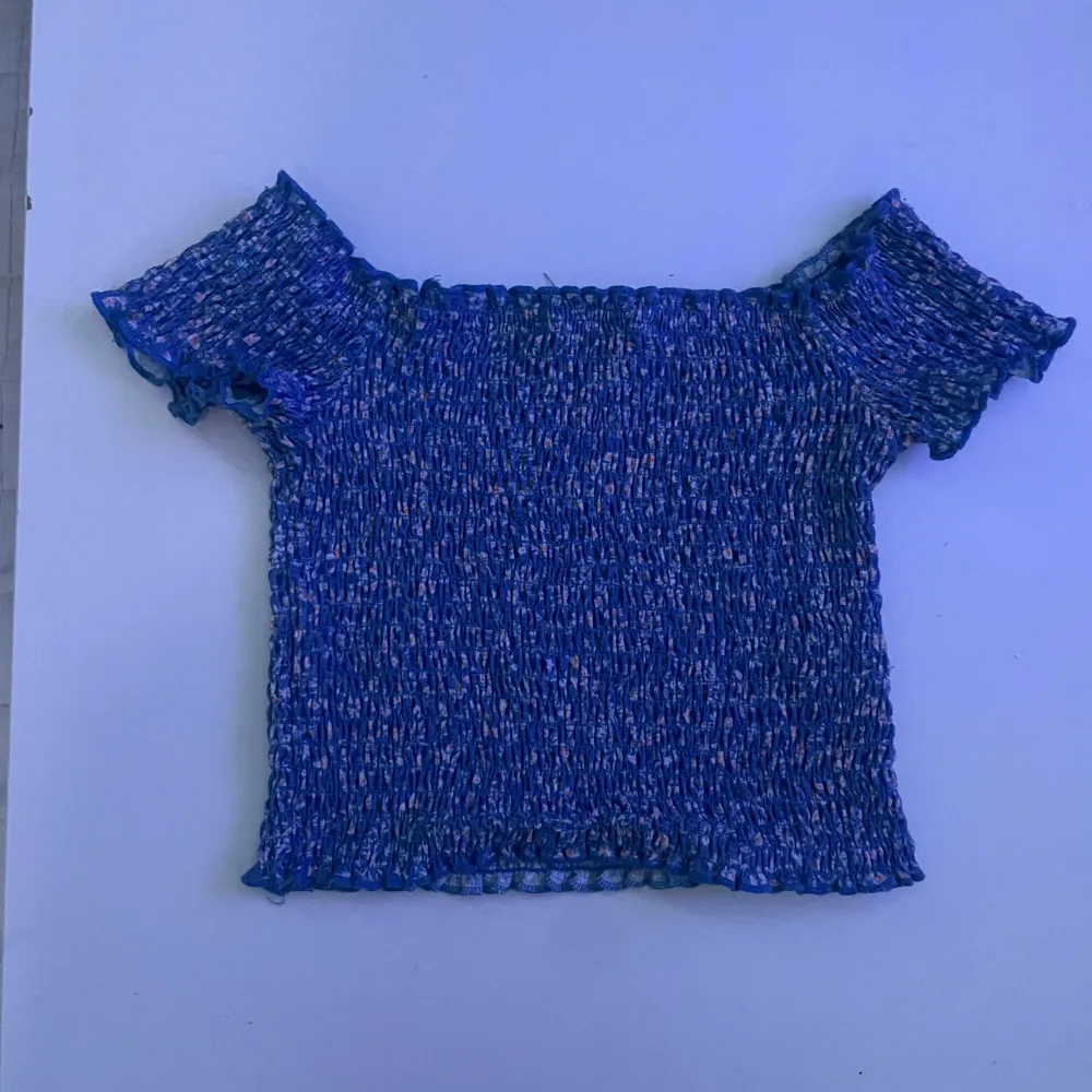 Säljer en söt blå offshoulder topp från Pull&Bear med blommigt mönster. Toppen är croppad och har en elastisk passform som ger en bekväm känsla. Perfekt för varma dagar!. Yläosat.