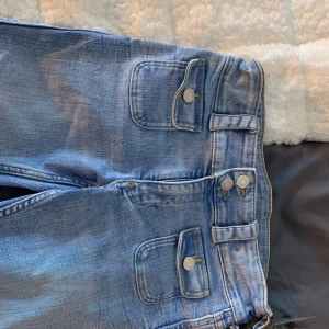 Blå jeans med dubbla knappar - Snygga blå jeans med dubbla knappar och unika fickdetaljer. De har en klassisk design med en modern twist och är perfekta för en avslappnad stil. Passar bra till olika outfits och tillfällen.