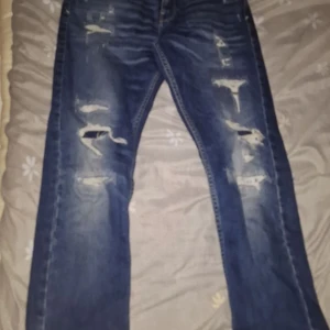 Blå jeans från Replay - Snygga blå jeans från Replay med slitna detaljer för en trendig look. De har en klassisk femficksdesign och en bekväm passform. Perfekta för en avslappnad stil. Strl 164-158