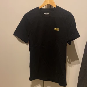 Svart t-shirt från Barbour - Snygg svart t-shirt från Barbour med en liten logga på bröstet. Den har en slim passform och är perfekt för en stilren look. Kortärmad och tillverkad i ett mjukt material.