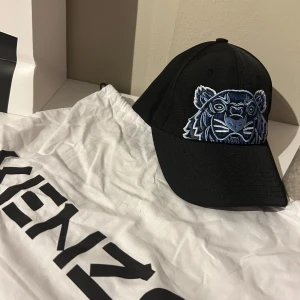 Svart keps med tigerbroderi från Kenzo - Snygg svart keps från Kenzo med ett coolt blått tigerbroderi på framsidan. Perfekt för att ge din outfit en trendig touch. Justerbar passform för optimal komfort.
