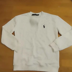 Vit tröja från Polo Ralph Lauren - Säljer en stilren vit tröja från Polo Ralph Lauren med det klassiska broderade logotypen på bröstet. Tröjan har långa ärmar och en bekväm passform. Perfekt för en avslappnad och snygg look.