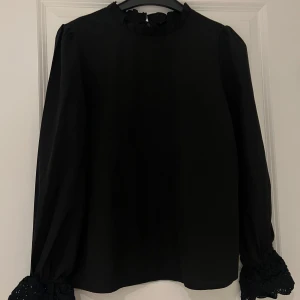 Svart blus med blommig design på armen - Svart blus med blommig design på armen från Shein. Har en design på kragen också. Använd en del och är på bra skick