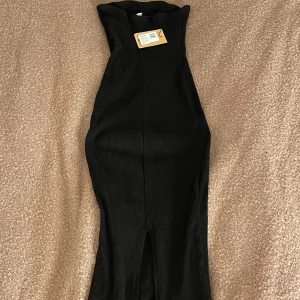 Svart ribbad klänning från Bershka - Snygg svart ribbad tubklänning från Bershka i en tight passform. Klänningen är axelbandslös och har en elegant lång design med slit där bak som passar perfekt för olika tillfällen. Perfekt nu inför sommaren. Köpt på Sellpy men oanvänd pga för stor. Prislappen är på❤️ Dm:a för frågor