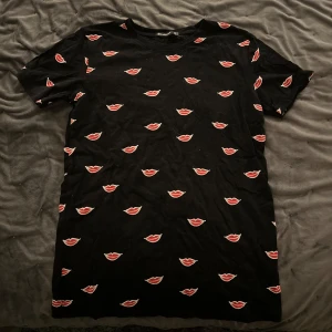 Svart t-shirt med läppmotiv från Stradivarius - Snygg svart t-shirt från Stradivarius med ett coolt läppmotiv i rött och vitt. Perfekt för en trendig look. Kortärmad och bekväm passform.