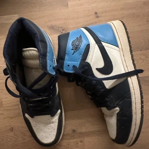 Nike Air Jordans 1 i blått och vitt - Snygga Nike Air Jordans i en fräsch kombination av blått, vitt och svart. Skorna har klassisk snörning och den ikoniska Air Jordan-loggan på sidan. Perfekta för dig som vill ha en stilren och sportig look.