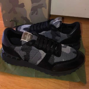 Valentino Garavani sneakers i camouflage - Snygga Valentino Garavani sneakers med ett coolt camouflagemönster i svart och grått. Skorna har snörning och en robust sula som ger bra grepp. Perfekta för dig som vill ha en stilren men ändå unik look. Storlek 43