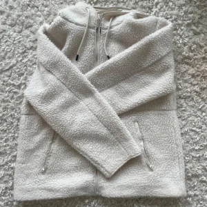 Teddyjacka - Vit teddyjacka med huva. Jackan har långa ärmar och två praktiska fickor med dragkedjor. Den värmer o säljer den för 270 kr (nypris 500). 