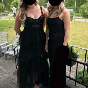 Svart långklänning med paljetter - Elegant svart långklänning med paljetter och volanger. Klänningen har en v-ringad design med breda axelband och flera lager av volanger i kjolen. Perfekt för en glamorös kväll. Använd endast en gång och med ett nypris på 4500kr