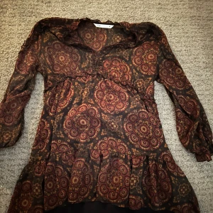 Mönstrad klänning från Zara - Snygg mönstrad klänning från Zara i mörka färger med mönster. Klänningen har långa ärmar och en volangdetalj vid fållen. Perfekt för en fin men inte för fin look.