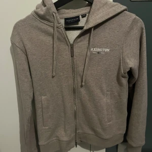 Beige hoodie från Lexington - Säljer en snygg beige hoodie från Lexington med dragkedja och huva. Perfekt för en avslappnad stil. Den har en liten Lexington-logga på bröstet och är tillverkad i ett mjukt material. Hoodie är nästan i helt ny skick använd då tals gånger utan defekter ny pris 1000 säljer den för endast 599. Passar typ 152-160