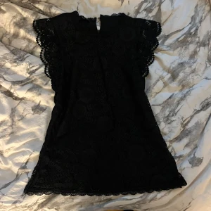 Svart spets blus - Säljer en elegant svart spetsblus med vackra detaljer. Blusen har korta ärmar med volang och en fin spetsdesign som ger en romantisk känsla. Perfekt för festliga tillfällen eller en utekväll. Passar bra till både sommar och höst.