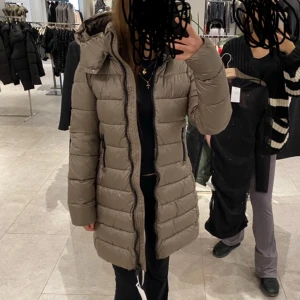 Beige dunjacka - Säljer en snygg beige dunjacka i mycket bra skick. Den är lång och har en dragkedja framtill. Perfekt för kalla vinterdagar med sin varma och sköna passform. Jackan har långa ärmar och en stilren design som passar till det mesta. 