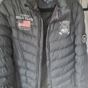 Svart quiltad jacka från Vinson Polo Club - Snygg svart quiltad jacka från Vinson Polo Club med broderade detaljer och dragkedja. Perfekt för kyligare dagar med sin stilrena design och bekväma passform.