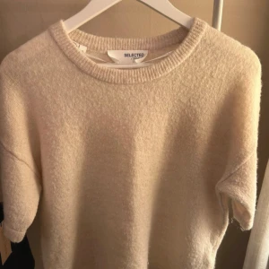 Beige tröja från Selected Femme - Mysig beige tröja från Selected Femme i en mjuk och fluffig textur. Perfekt för kyligare dagar med sin kortärmade design och rund halsringning. En stilren och enkel baströja för garderoben.
