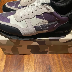 Valentino Garavani sneakers i kamouflage - Snygga Valentino rockrunners med kamouflagemönster i lila, beige och svart. Skorna har lite repor på fram sidan men märks inte så jätte mycket. Skriv vid fundering, pris kan diskuteras.