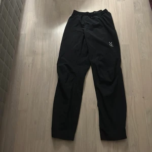 Svarta byxor från Haglöfs - Säljer ett par svarta byxor från Haglöfs i storlek herr S. Byxorna har en elastisk midja och är perfekta för utomhusaktiviteter. De är tillverkade i ett slitstarkt material och har en diskret logga på benet.