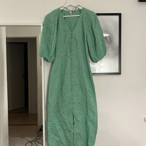 Grön klänning med puffärmar - Snygg grön klänning med puffiga trekvartsärmar och ett diskret hålmönster. Perfekt för vår och sommar. Klänningen har en v-ringad hals och en elegant passform.